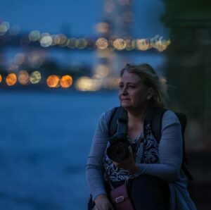 Martine Poulain, appareil photo en main, pont de Manhattan de nuit en fond